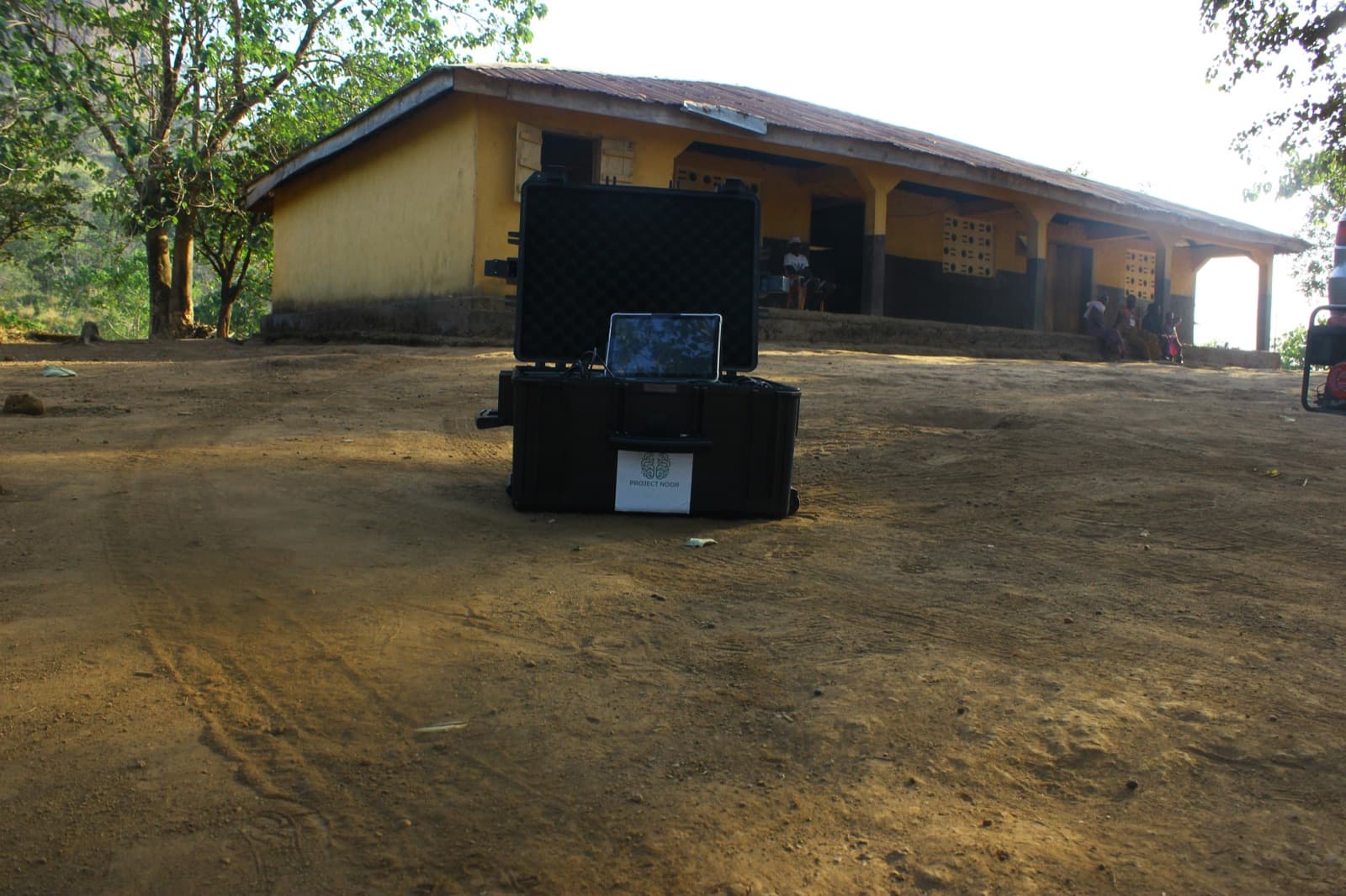 The open Project Noor case on red dirt in front of the village school.